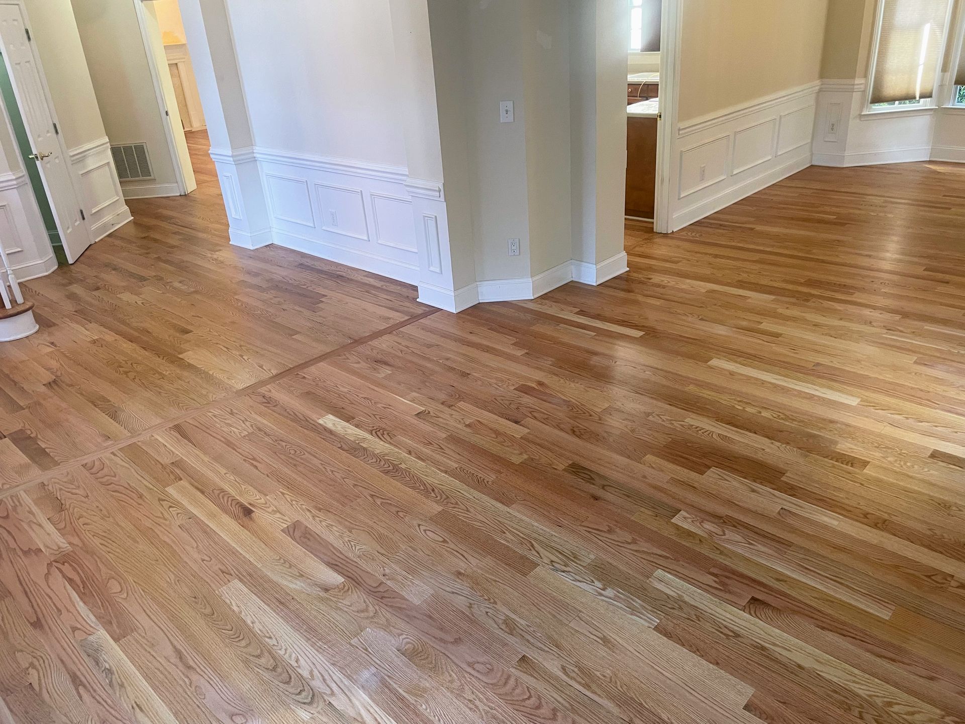 Hardwood floor with off-white walls, molding, and an open doorway. The floor is light brown, and the walls have a beige hue.