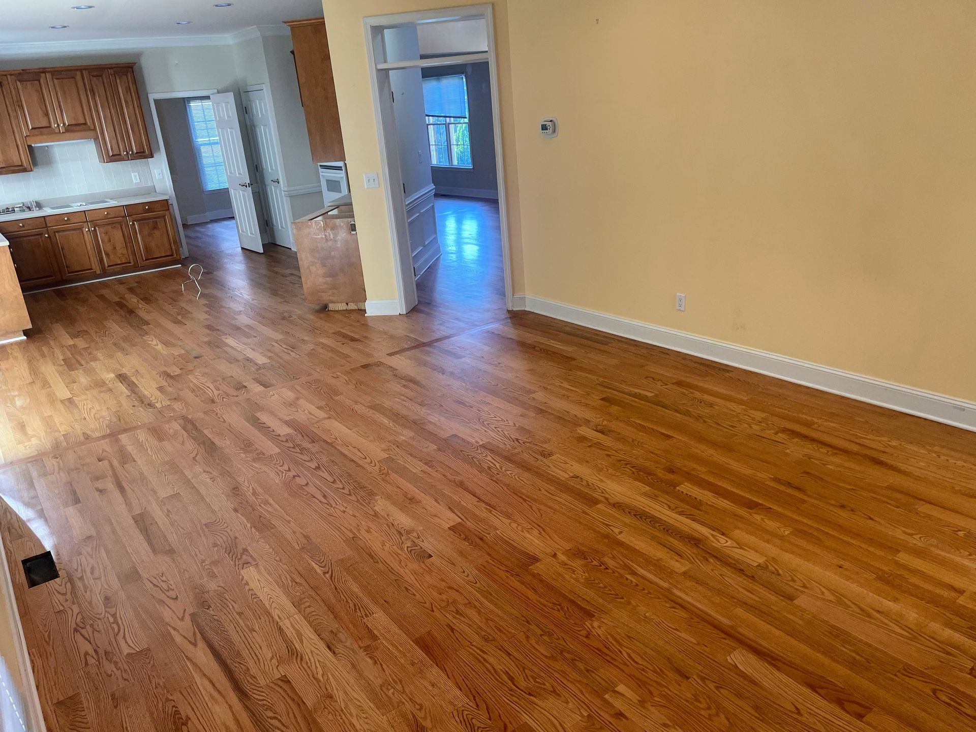 Hardwood floors extend from the kitchen to an entry door. Light brown cabinets and yellow wall present.