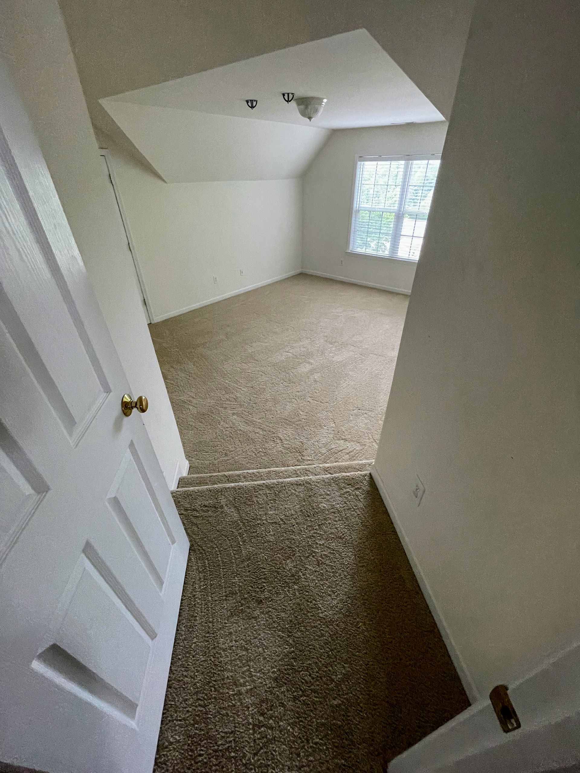 Open doorway leads to a bedroom with carpeted floor, window, and sloped ceiling.