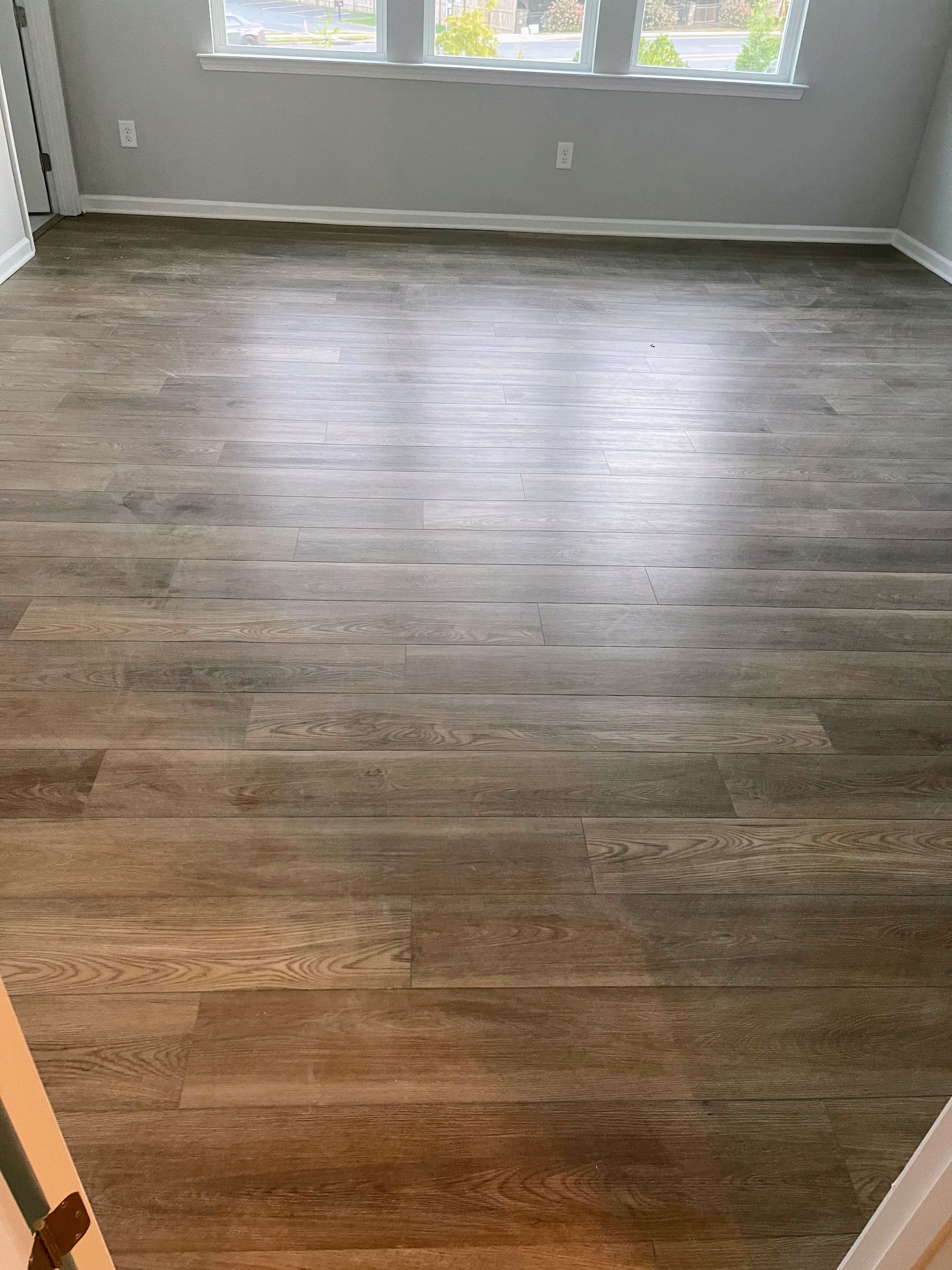 Wooden floor in a room, reflecting light from a window in the background.