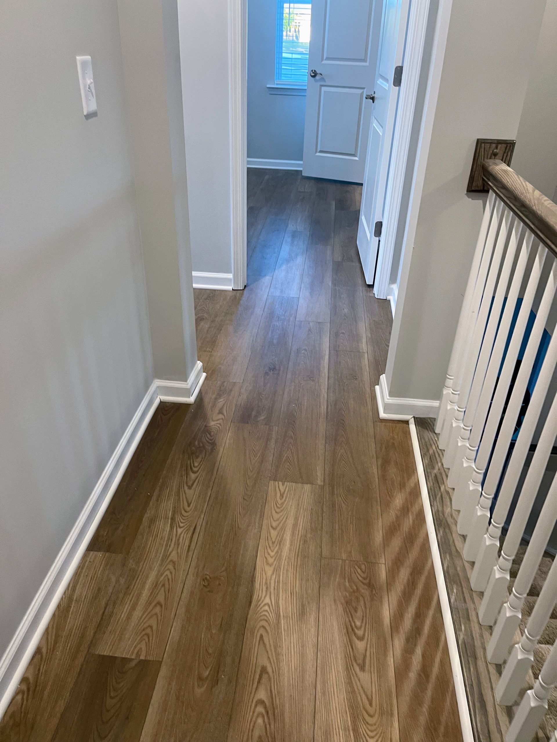 Hallway with wooden floor, white trim, grey walls, and a staircase railing.