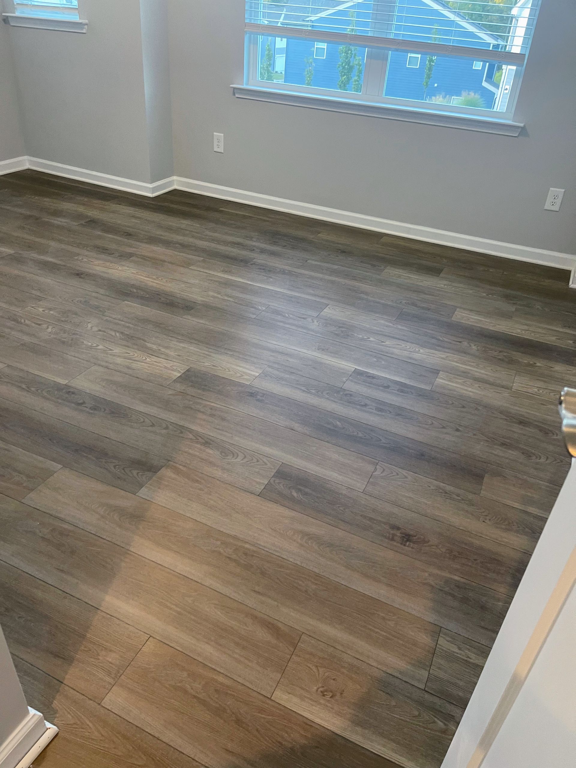 Wood-look flooring in a room with a window, white trim, and gray walls.