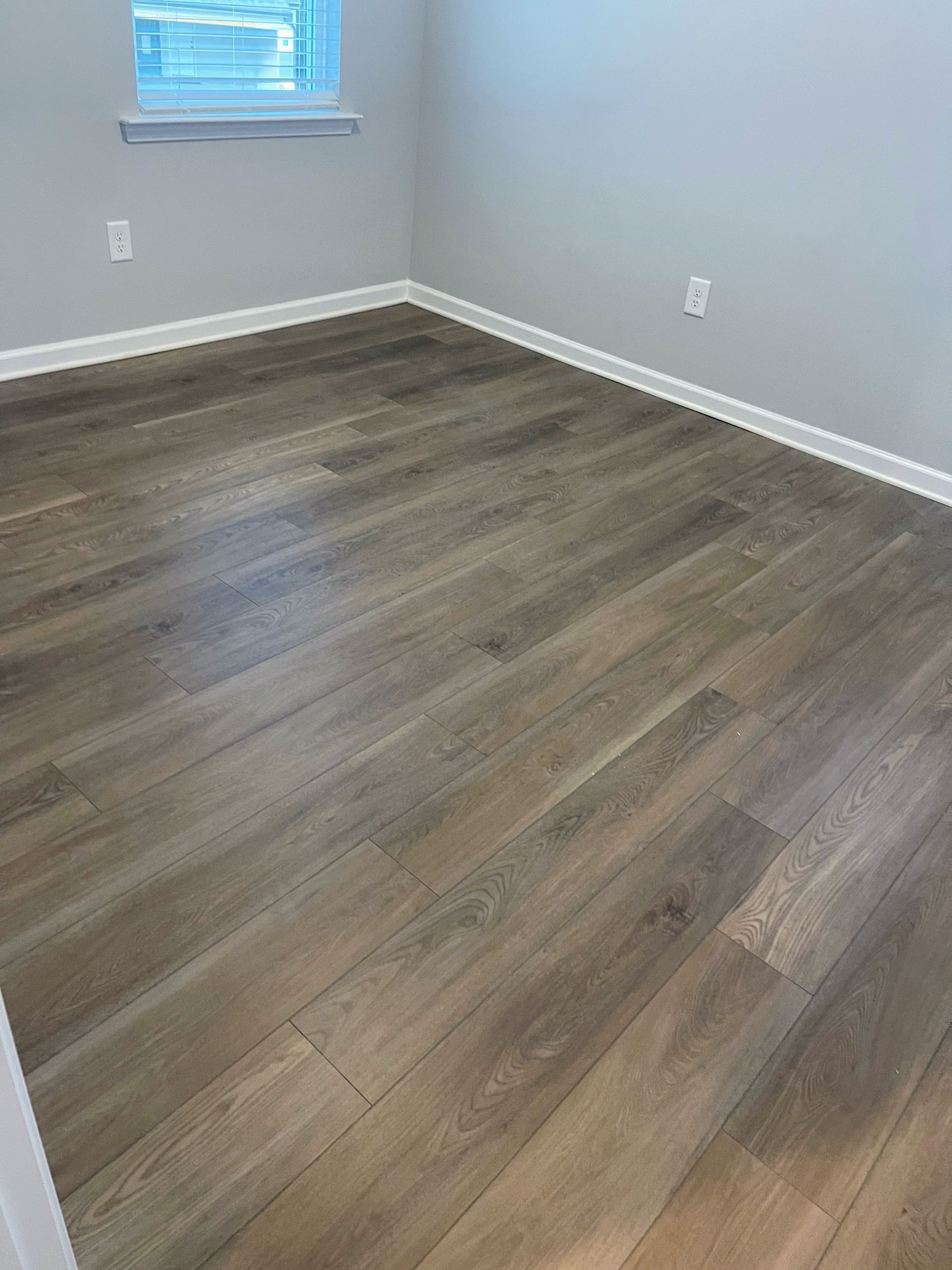 Empty room with gray walls and wood-look flooring. A window is in the background.
