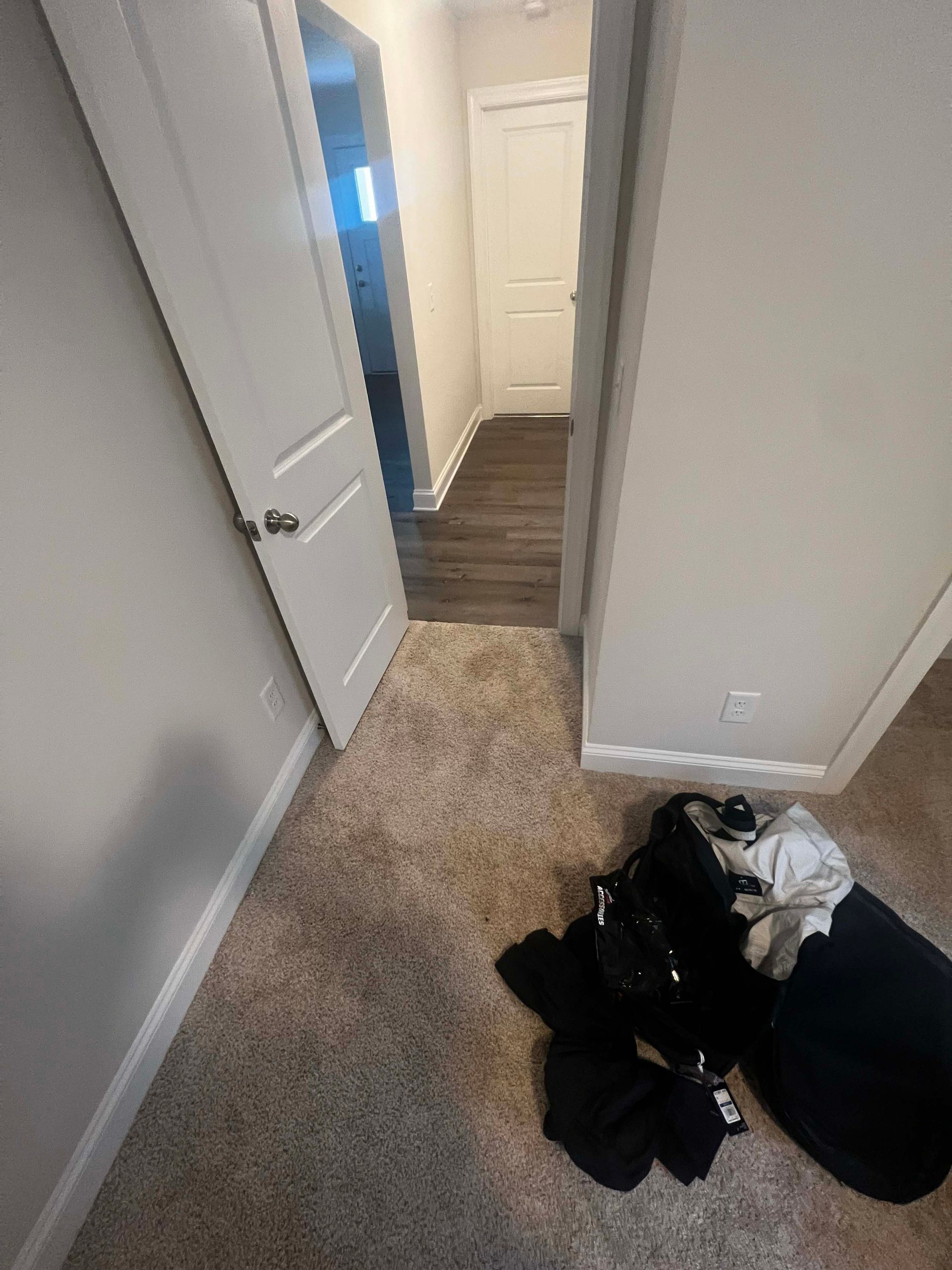 Hallway with carpet and dark floor, two doors, clothes on the floor, and neutral walls.