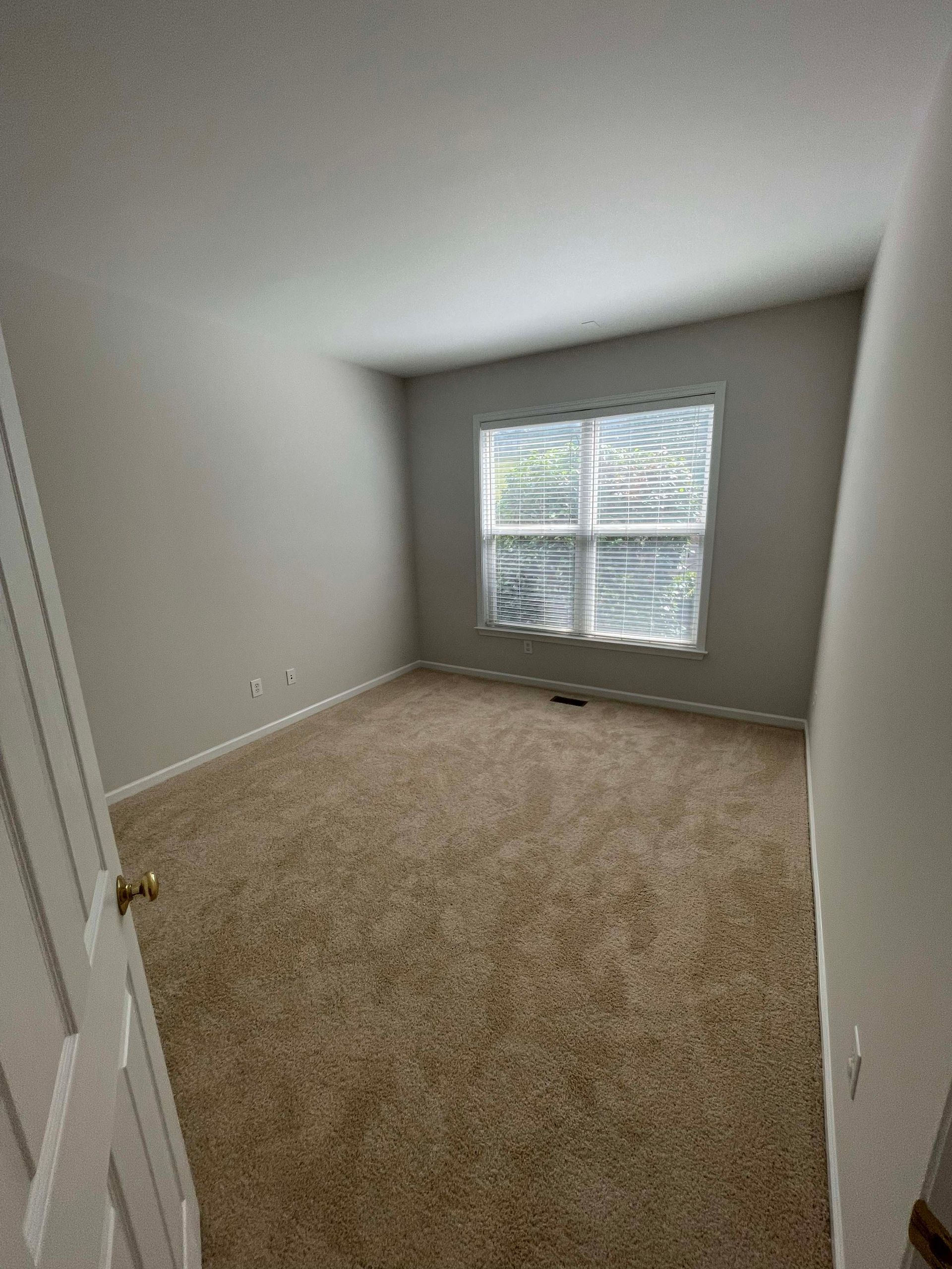 Empty room with beige carpet, window with blinds, and light gray walls.