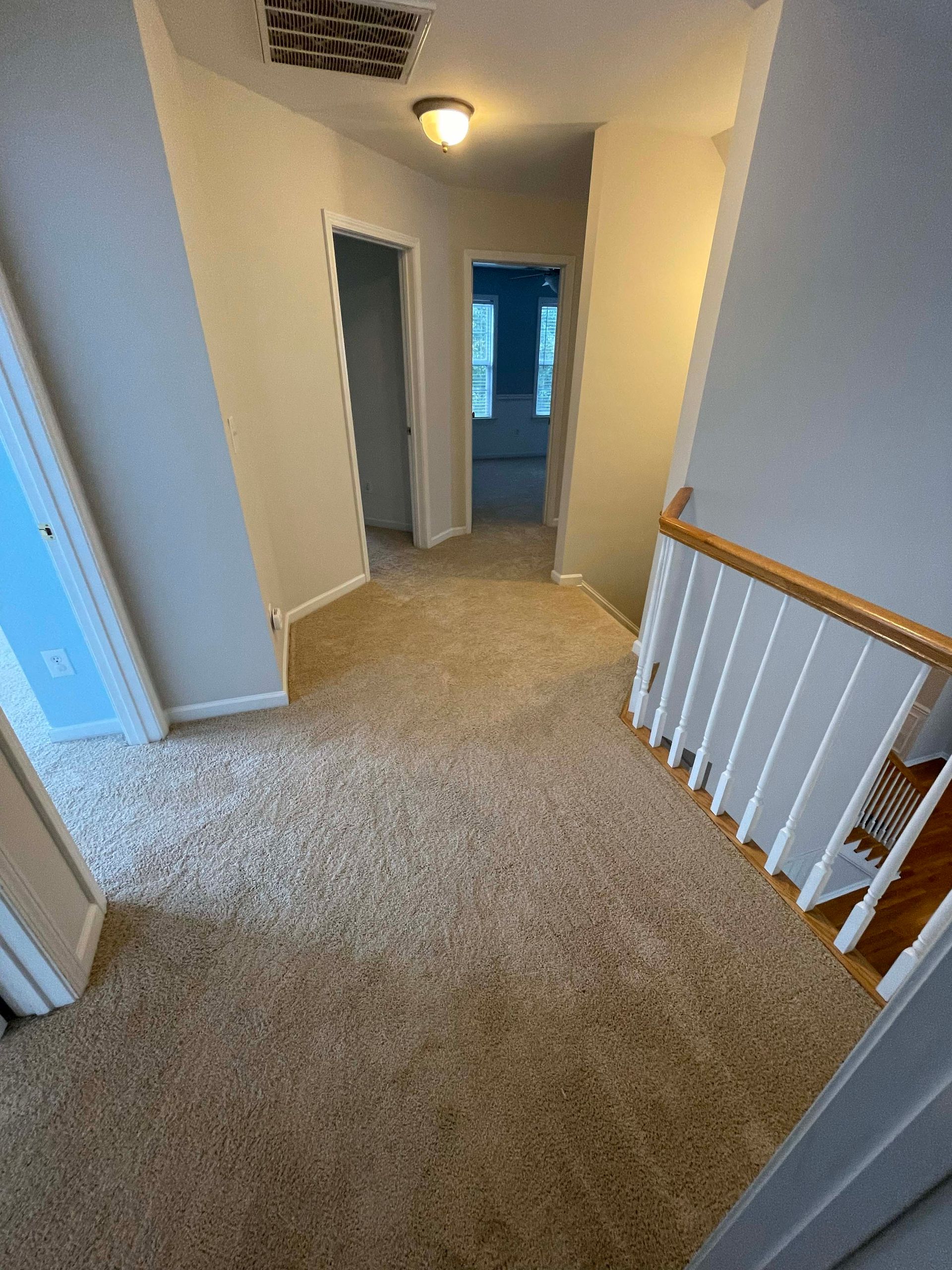 Hallway with beige carpet, doors, and a staircase with a white railing and wooden handrail.