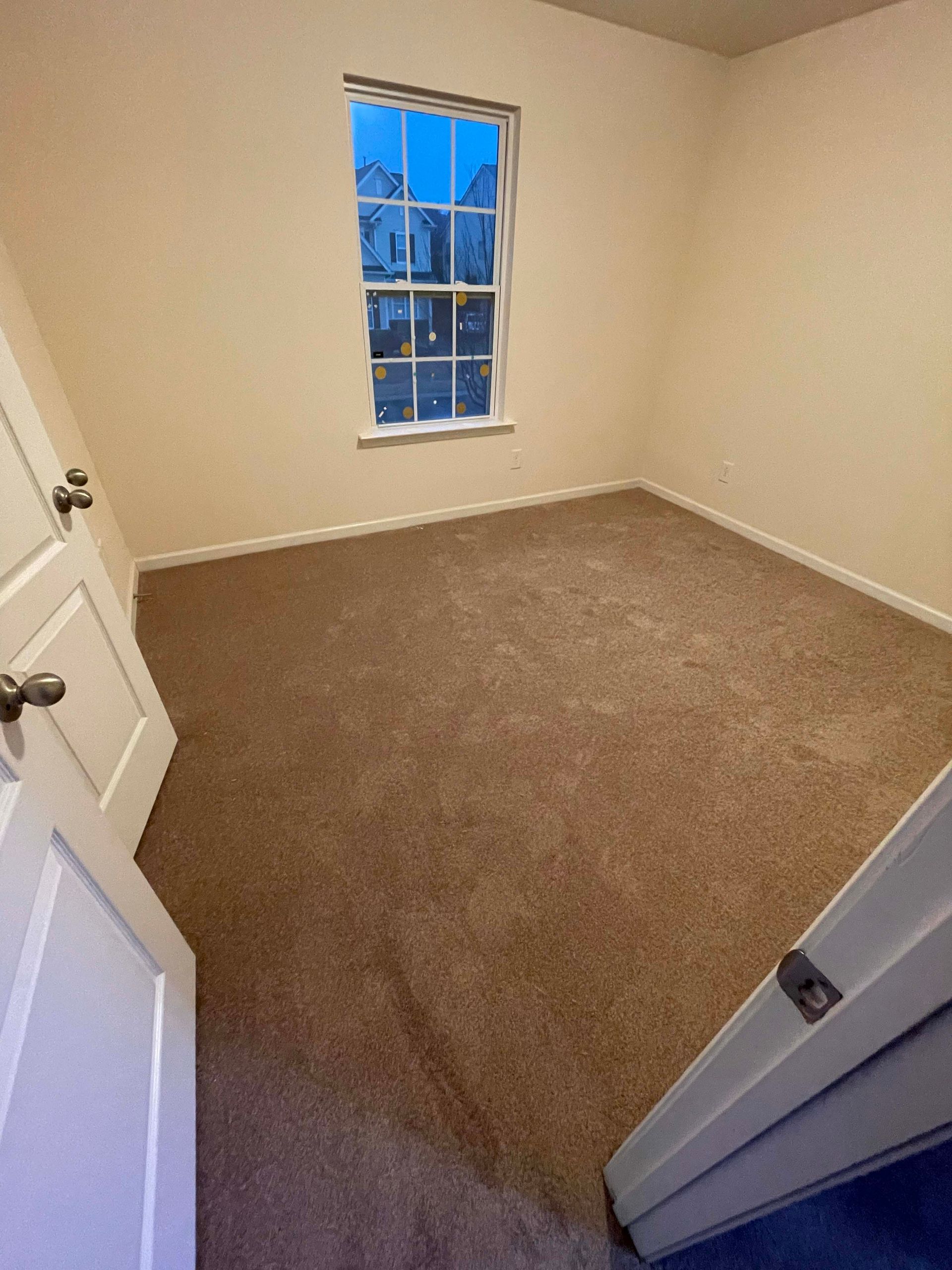 Empty room with tan carpet, a window, and two white doors.