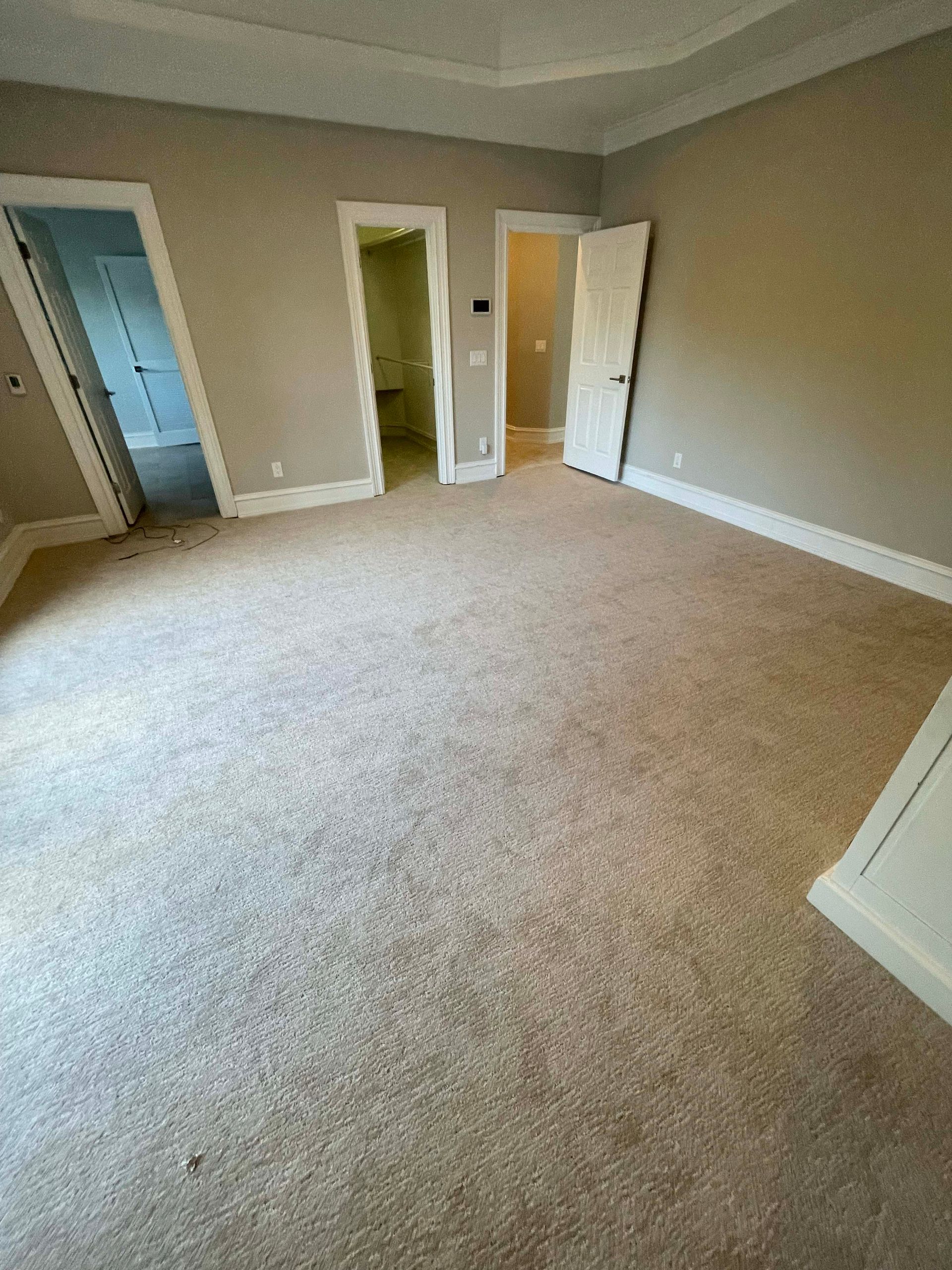 Empty bedroom with carpet, three doorways, and beige walls.