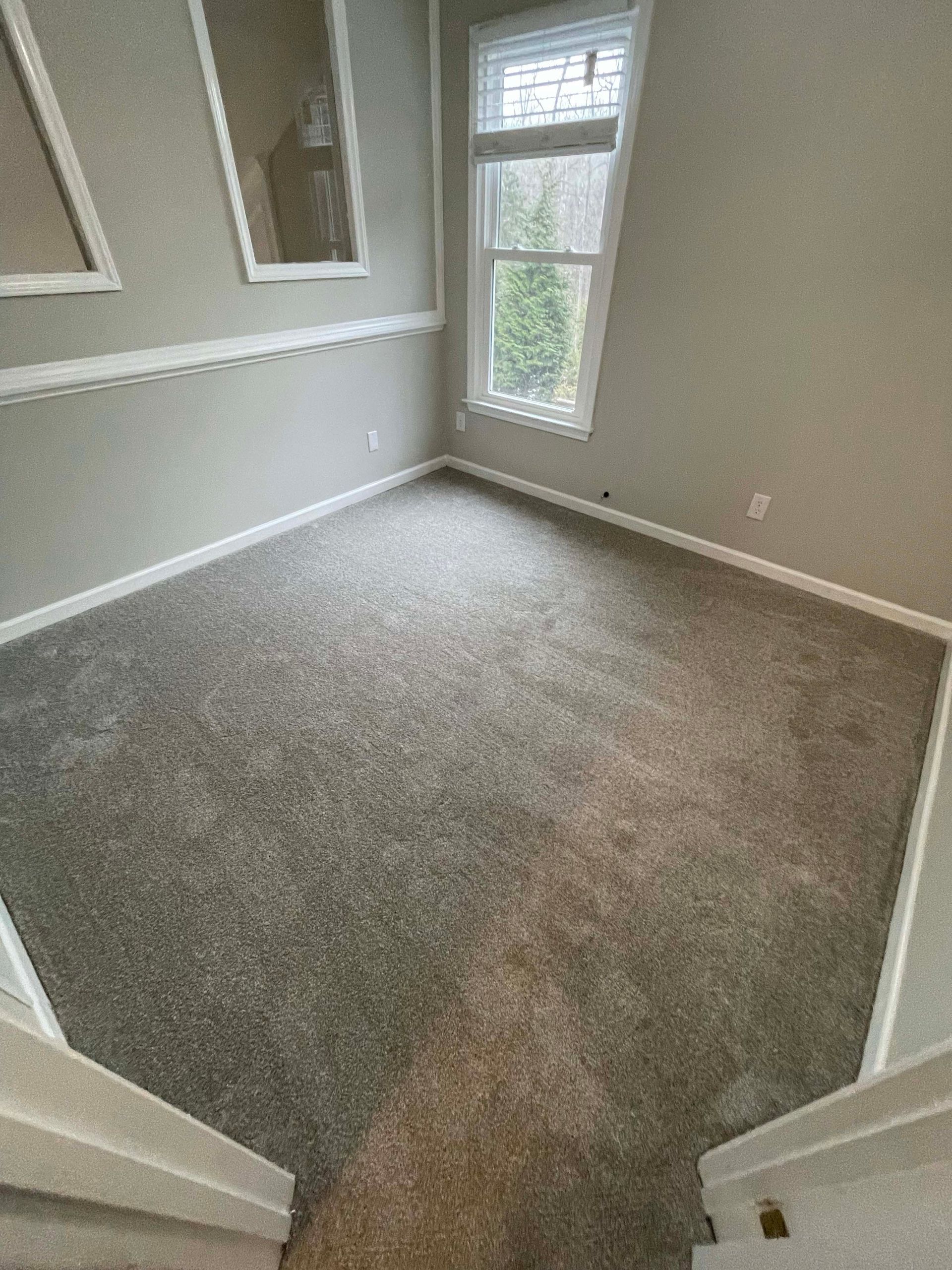 Empty room with gray carpet, window, and two framed wall mirrors.
