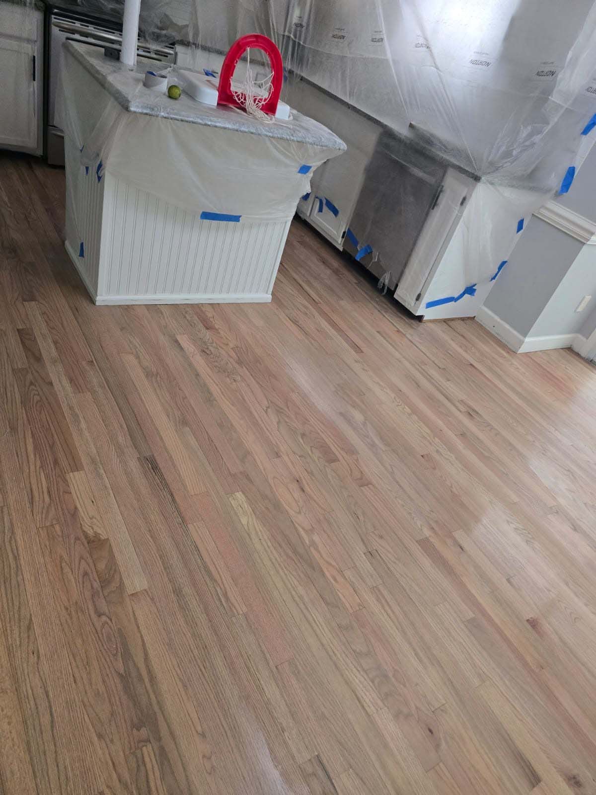 Newly installed hardwood floors in a kitchen with protected countertops and appliances.