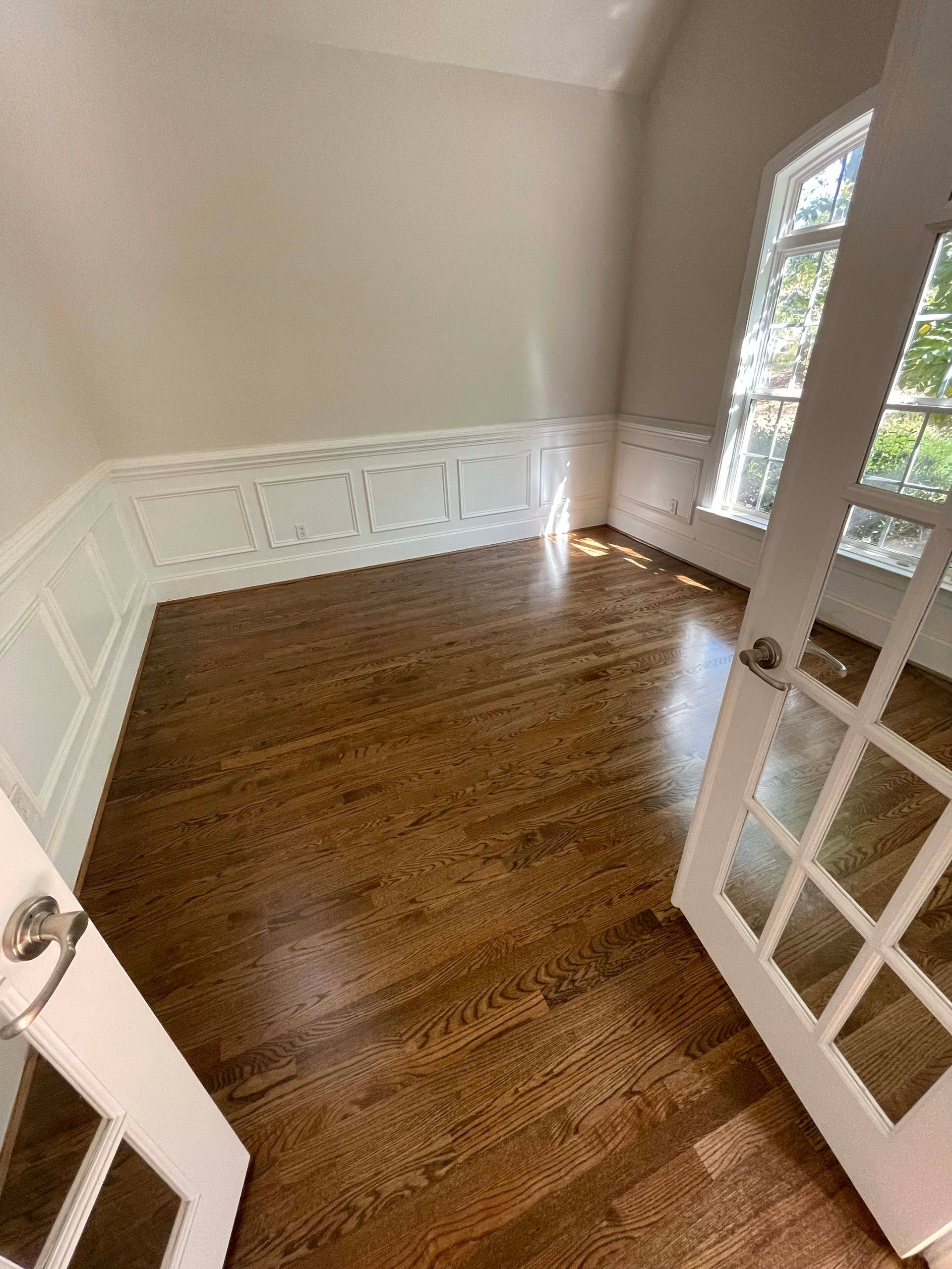 Empty room with wood floors and white paneling. French doors and a window are visible.