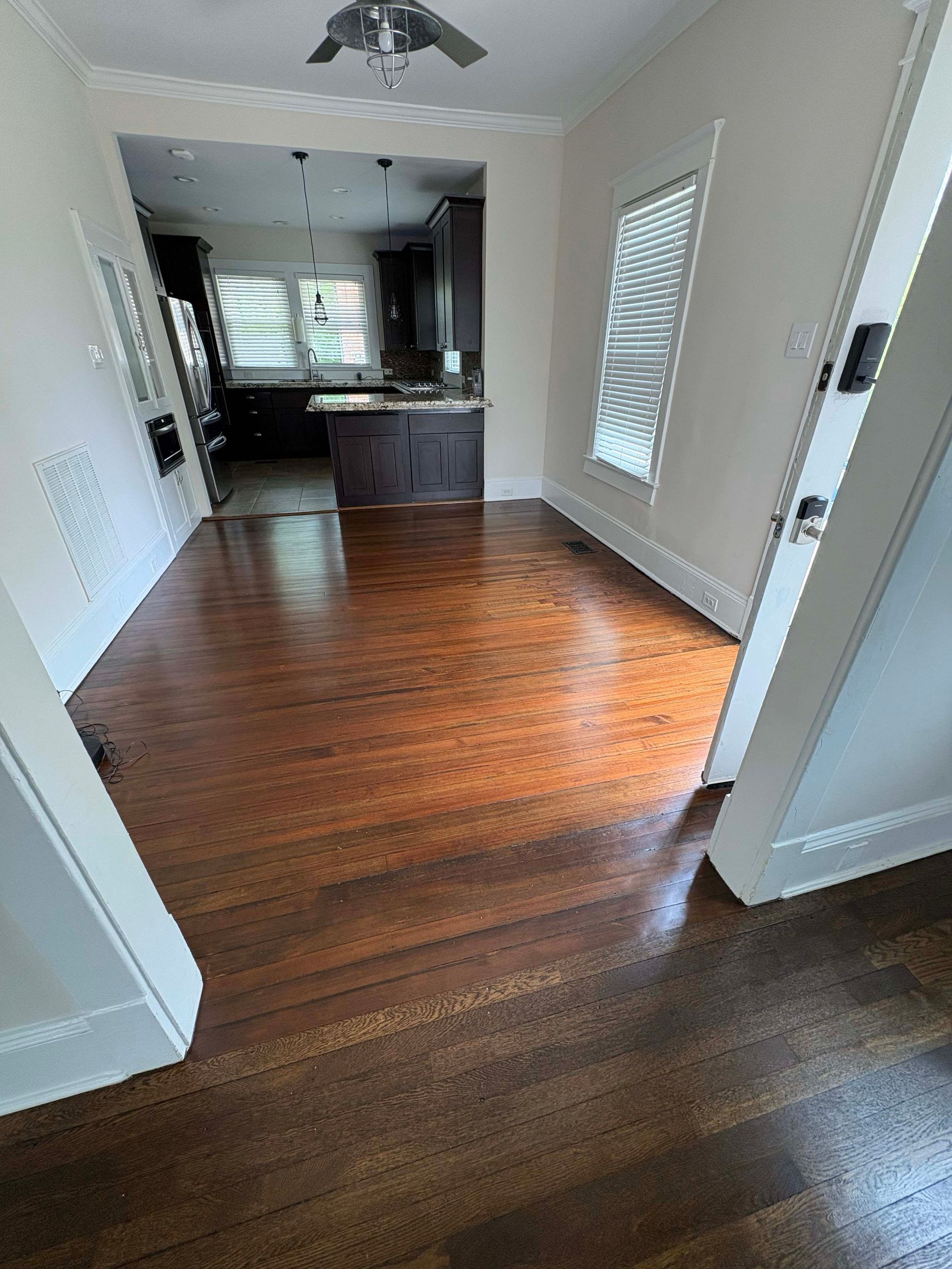 View through a doorway into a dining area with dark hardwood floors, leading toward a kitchen with dark cabinetry.