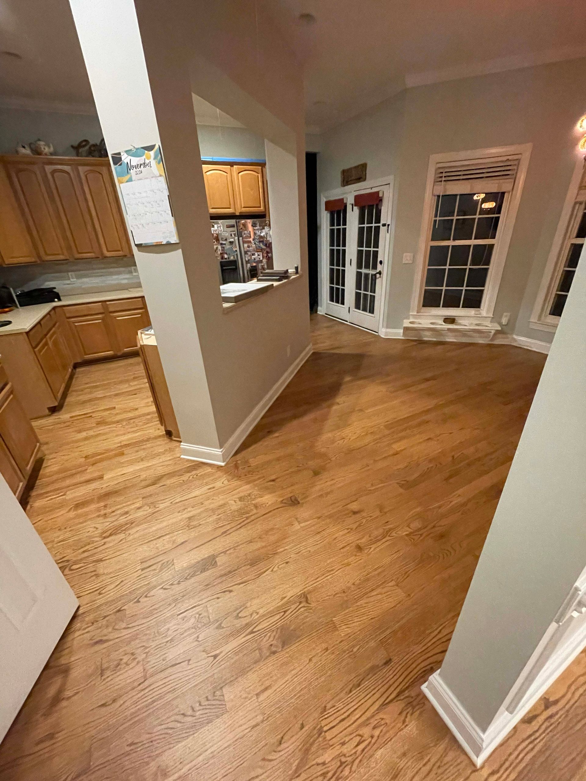 A hardwood-floored room featuring a kitchen pass-through window, light wood cabinets, French doors, and two large windows.