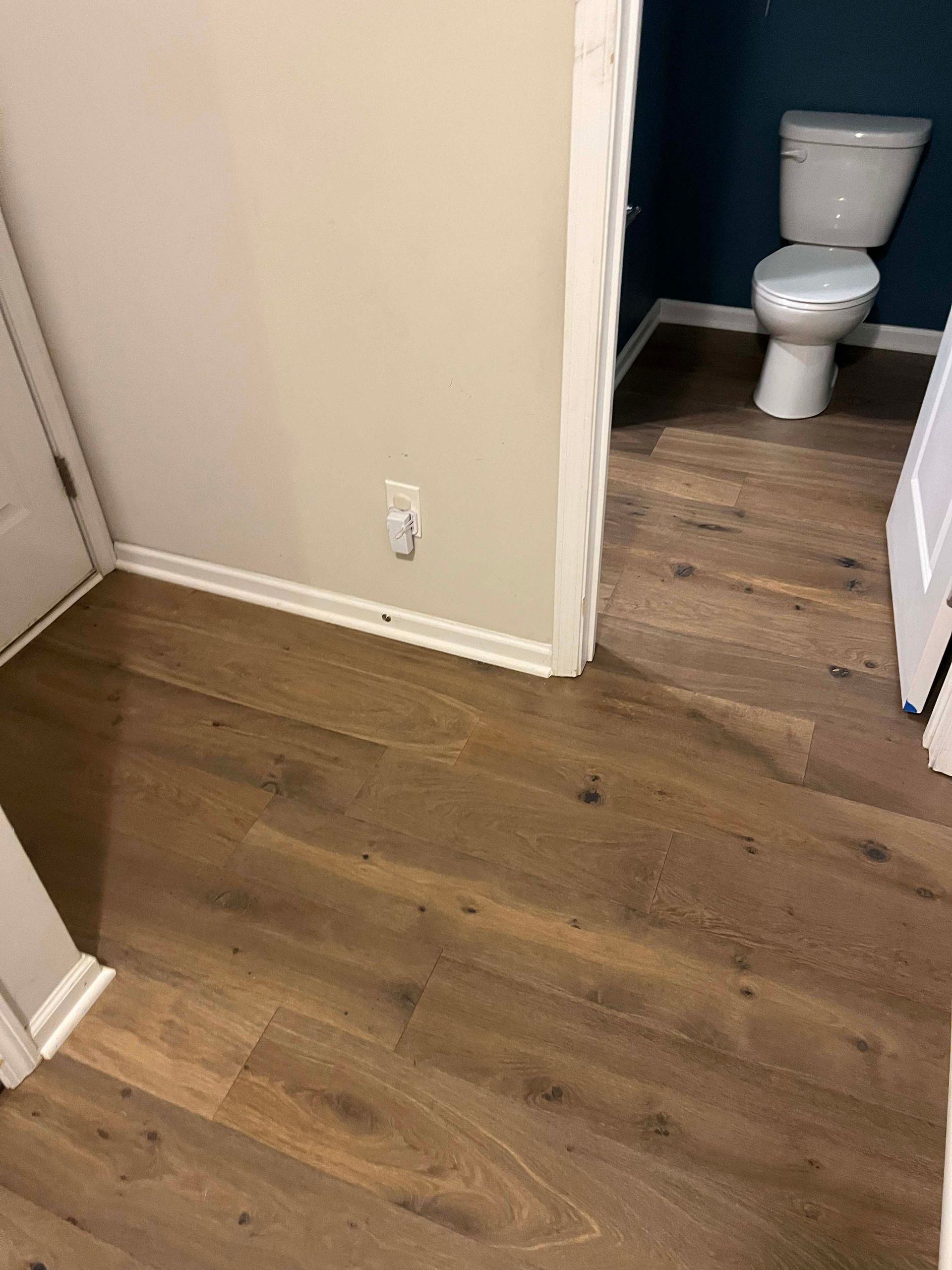 Wooden floor leads to a bathroom with a white toilet and teal wall. Beige walls and white trim.