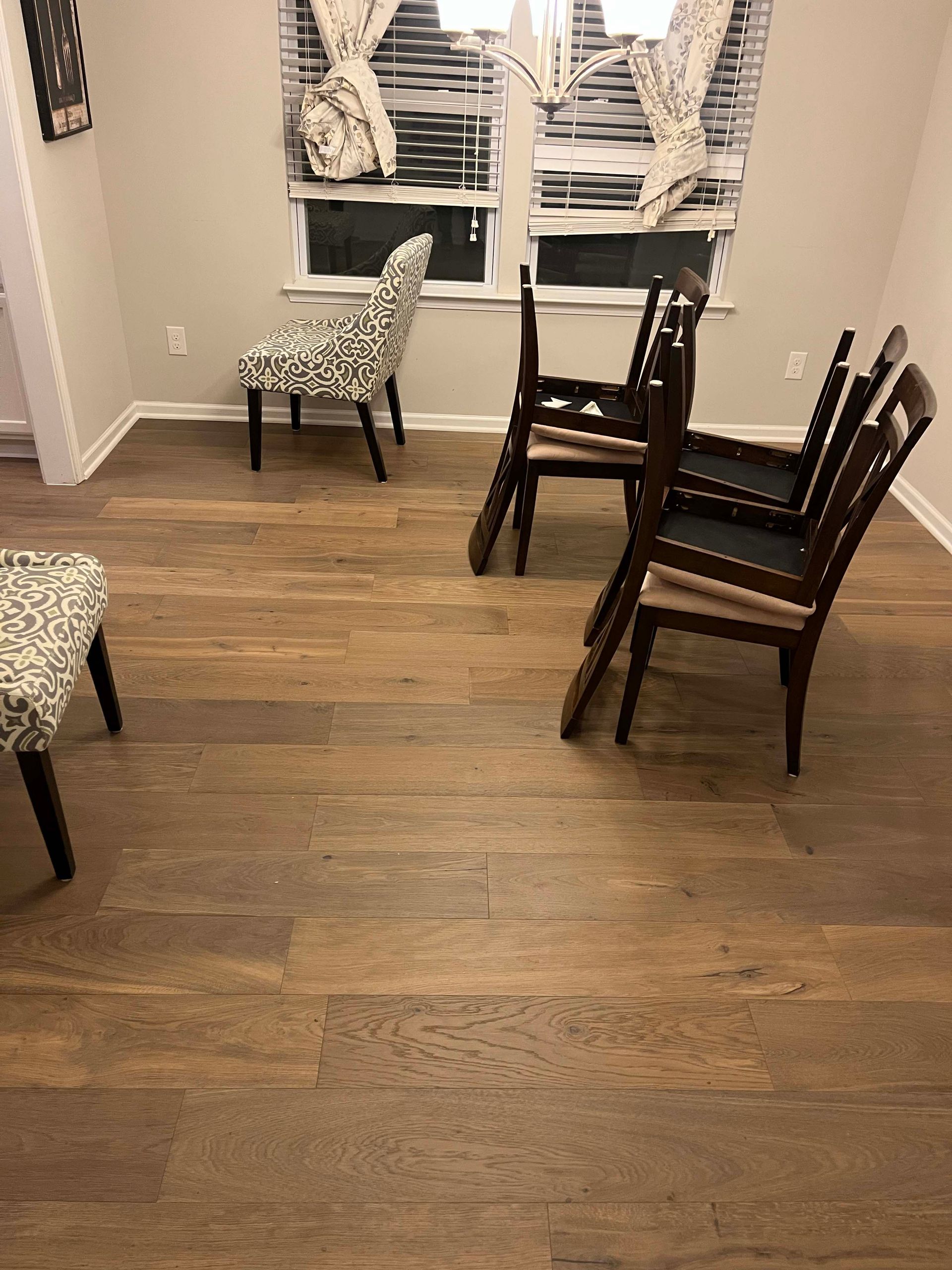 Hardwood floor in room with mismatched chairs near window.