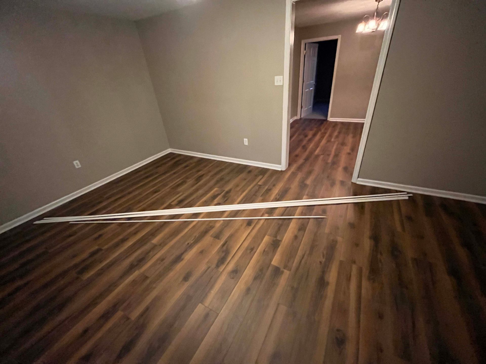 Empty room with dark wood-look flooring and light gray walls; open doorway to hallway.