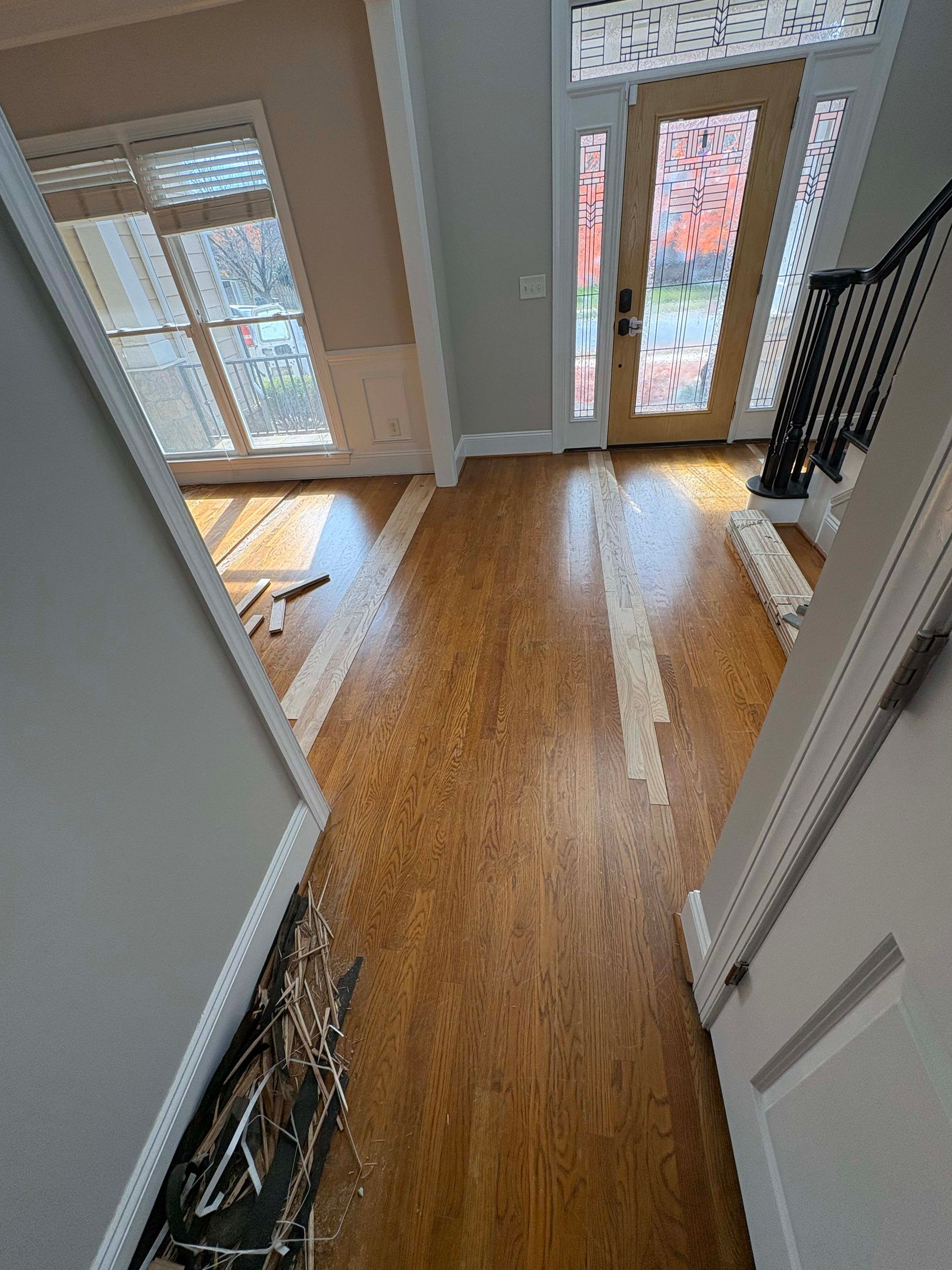 Entryway with hardwood floors, light gray walls, a wooden front door, and a staircase with a black railing.