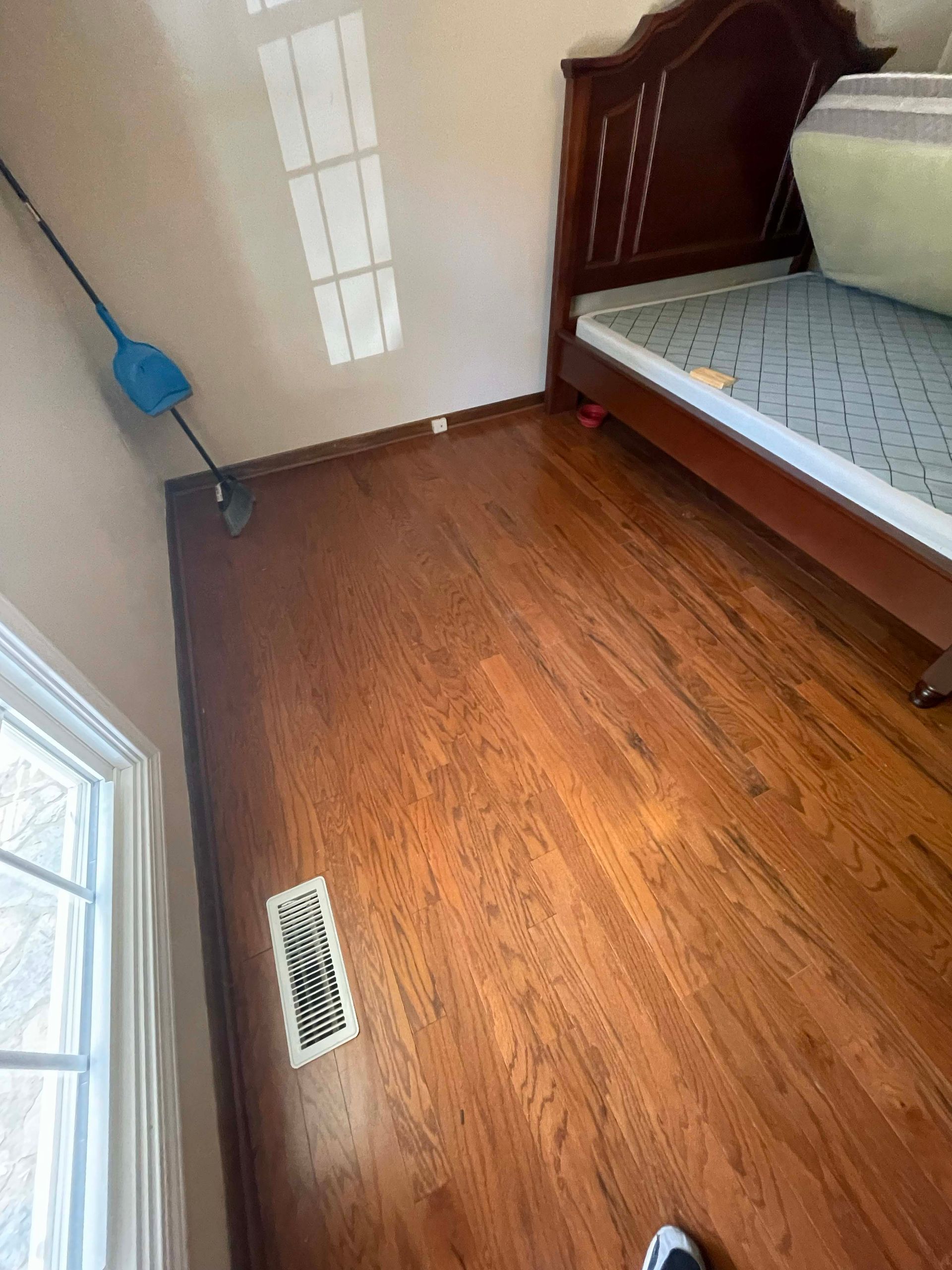 Bedroom with hardwood floors, a bed, window, and a broom leaning against the wall.