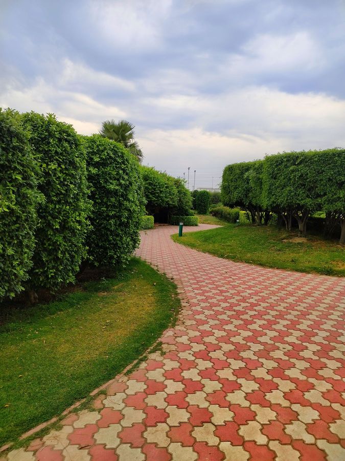 Curved red-and-cream brick path through green hedges under a cloudy sky