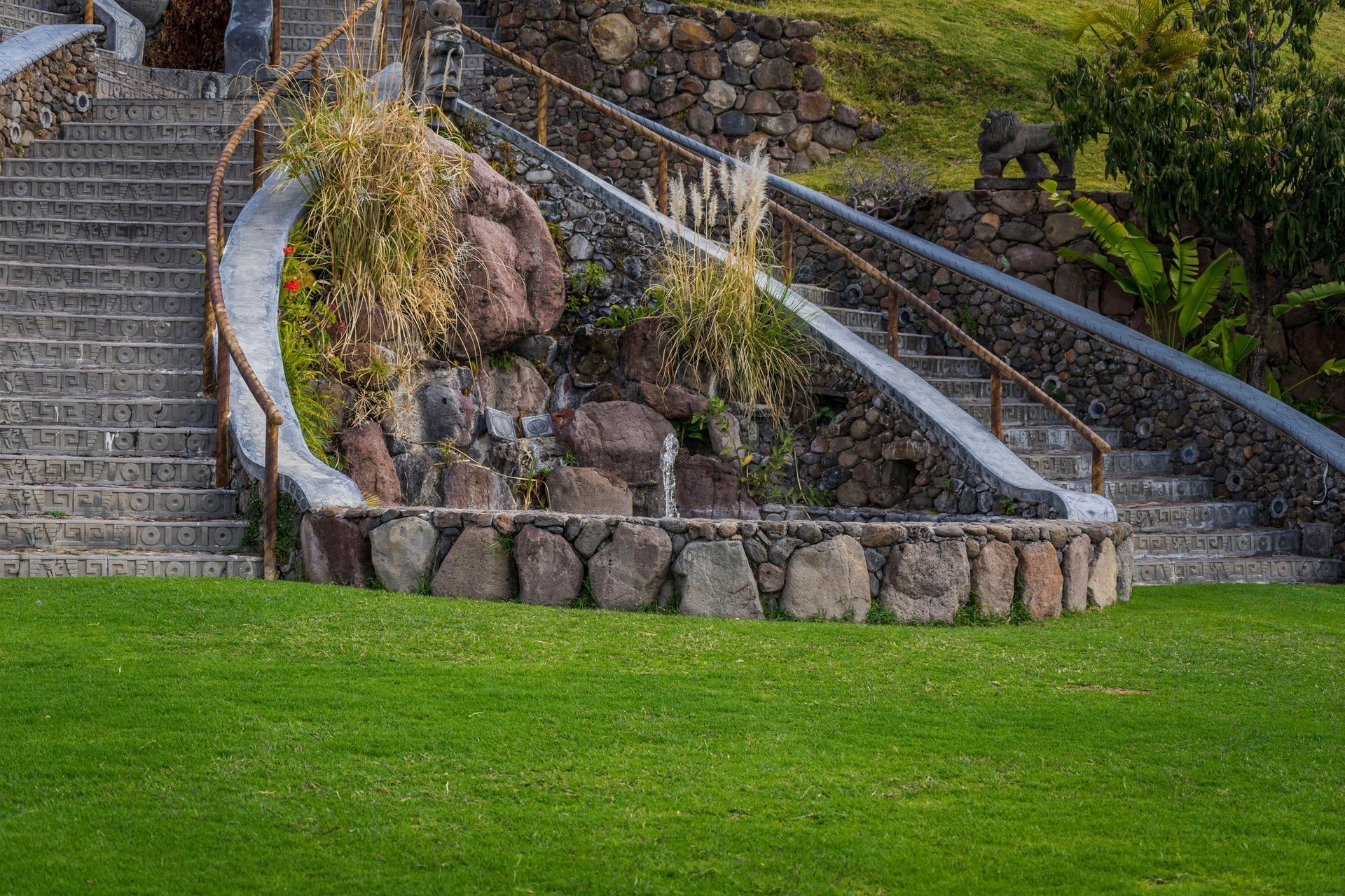 Stone staircases curve around a rocky landscaped mound beside a green lawn.
