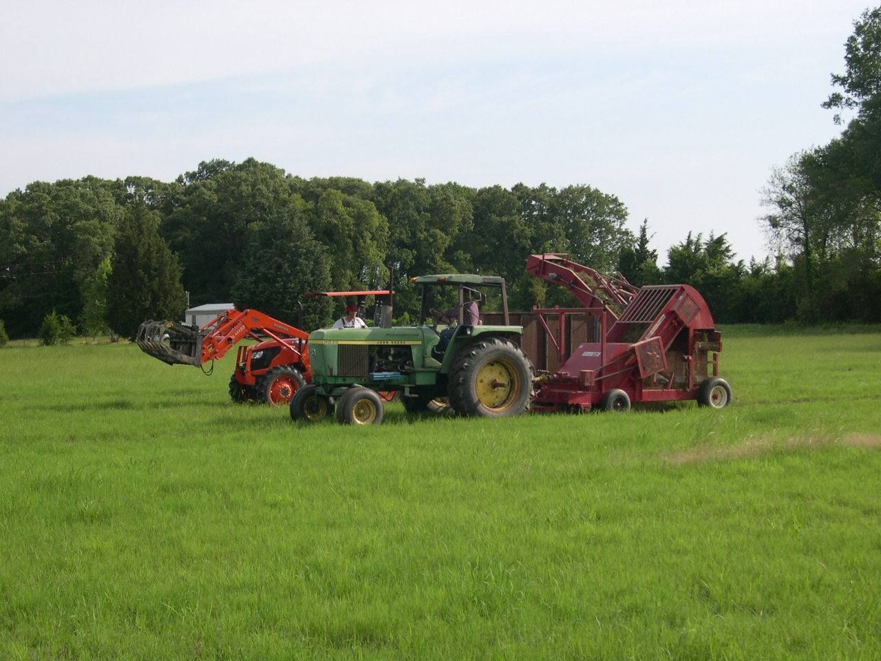 Tractors and farm equipment in a green field with trees in the background