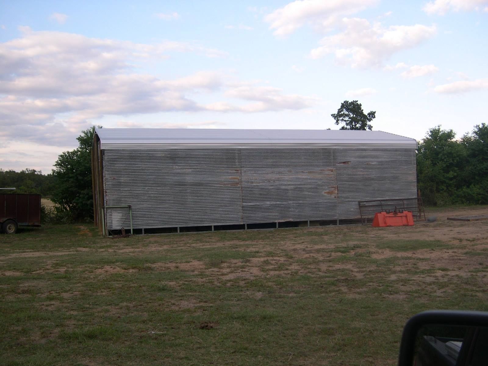A large gray tarp-covered structure in a grassy field under a cloudy sky.