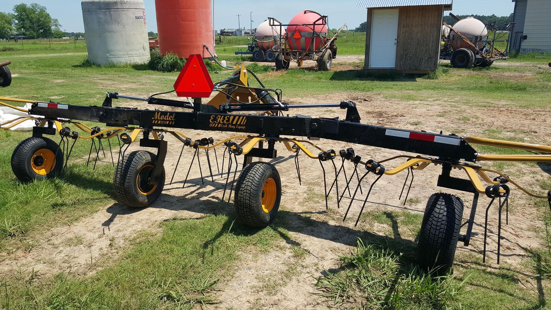 Farm equipment in a field: a black hay rake with yellow wheels and a red slow-moving triangle marker.