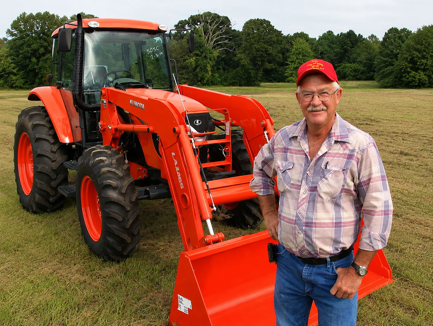 Two people standing beside an orange tractor in a grassy field, smiling at the camera.