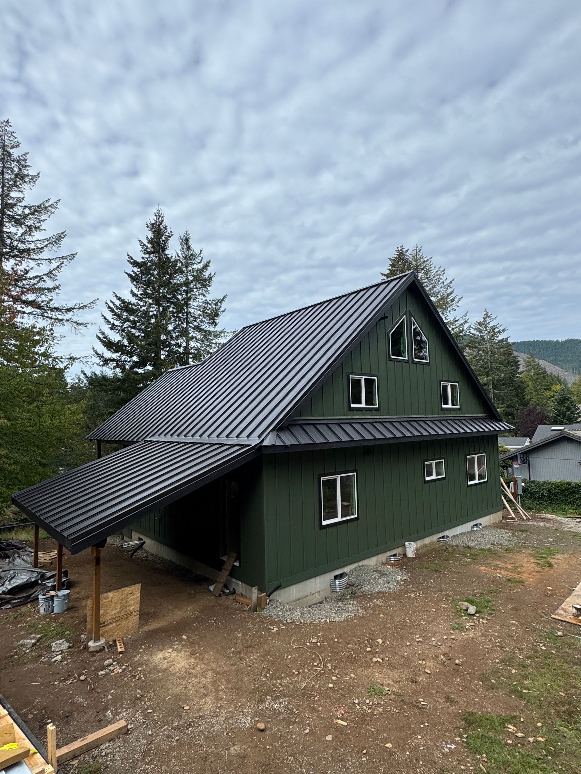 Green cabin with black roof and awning, windows. Overcast day.