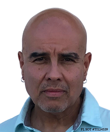 Portrait of a bald man with earrings and a goatee, wearing a light blue collared shirt against a white background