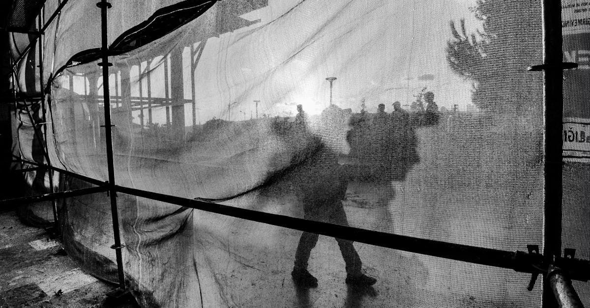 People behind a netted fence in a smoky black-and-white scene, one person leaning forward.