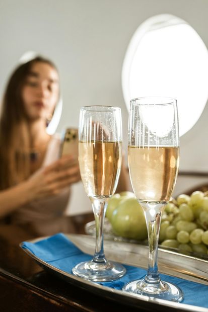 Two champagne flutes on a blue tray with grapes and a woman blurred in the background