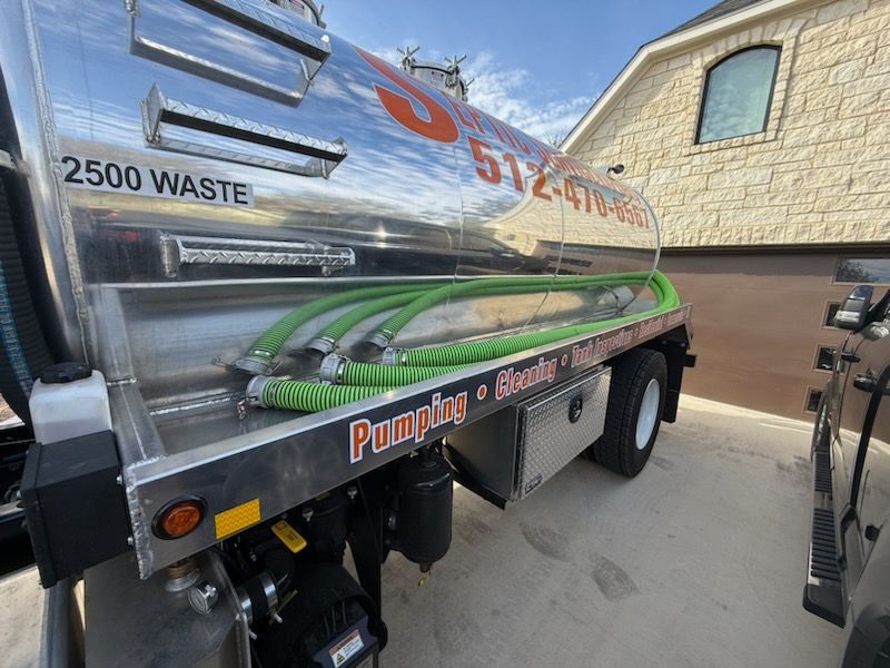 Septic pumping truck with chrome tank and green hoses, parked near a light-colored house.