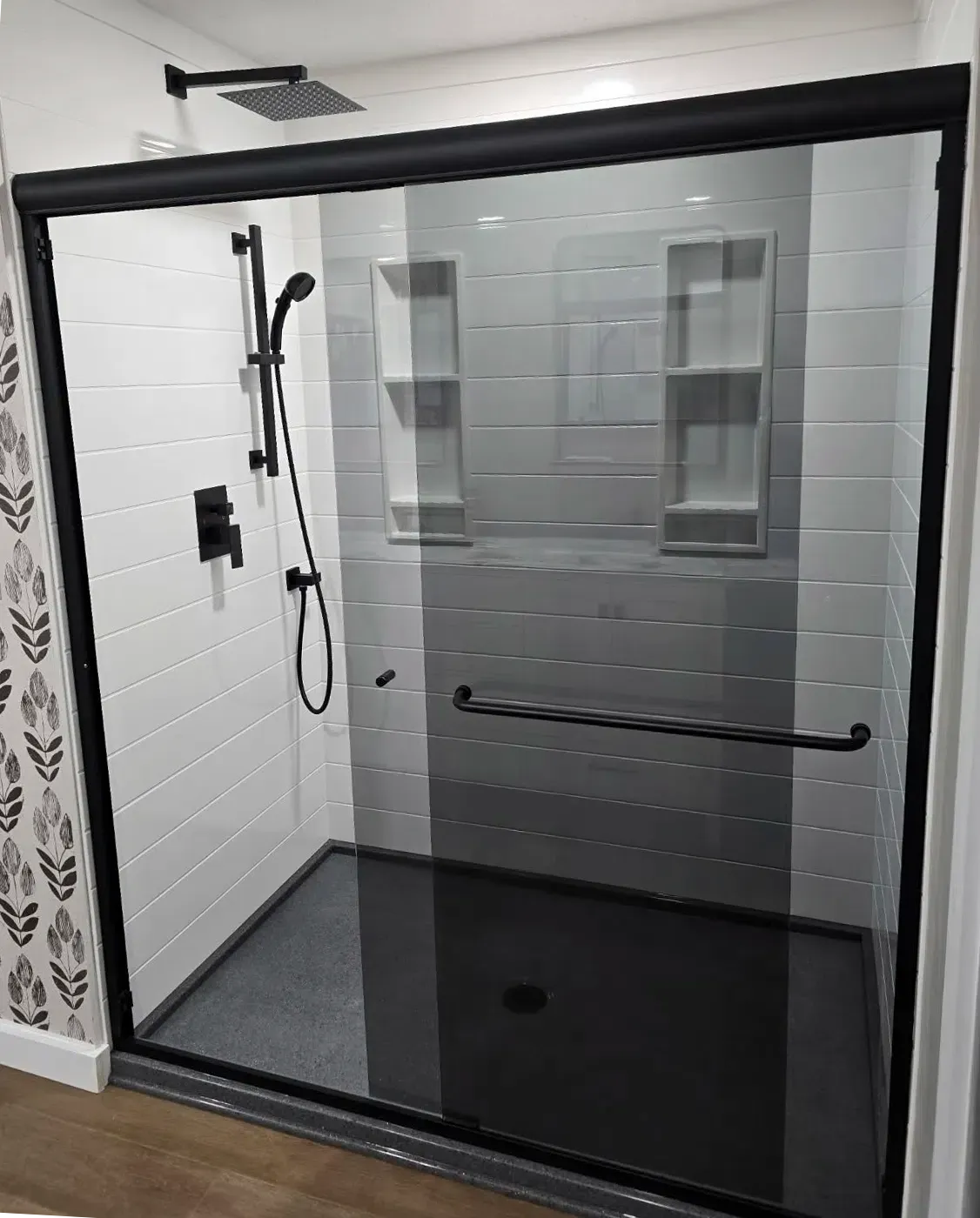 A modern, neutral-toned bathroom featuring a walk-in glass shower enclosure, a bathtub, and an open wooden vanity.