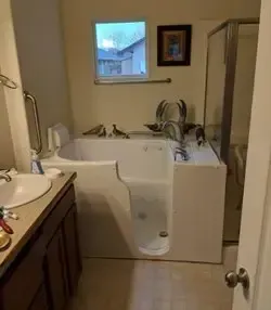 A walk-in bathtub with a side-access door, situated in a residential bathroom with a vanity and shower enclosure.