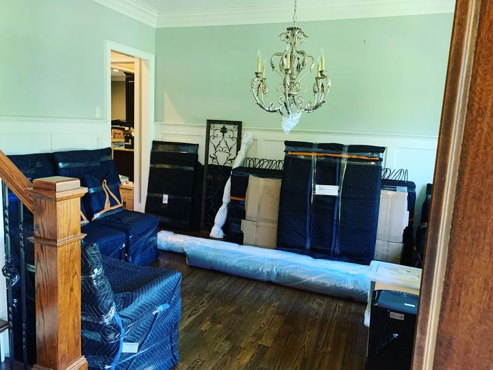 Living room with stacked furniture, wrapped items, chandelier, and hardwood floor during a move.