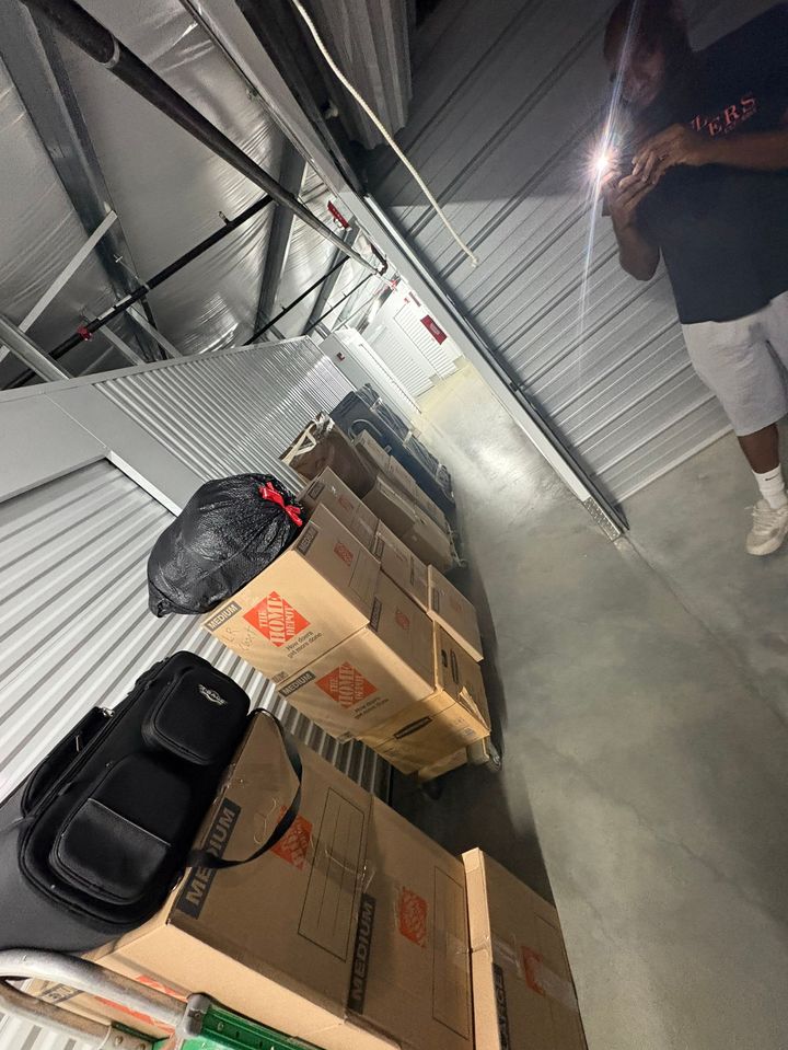 Storage corridor with stacked cardboard boxes and black bags along a metal wall, viewed at an angle.