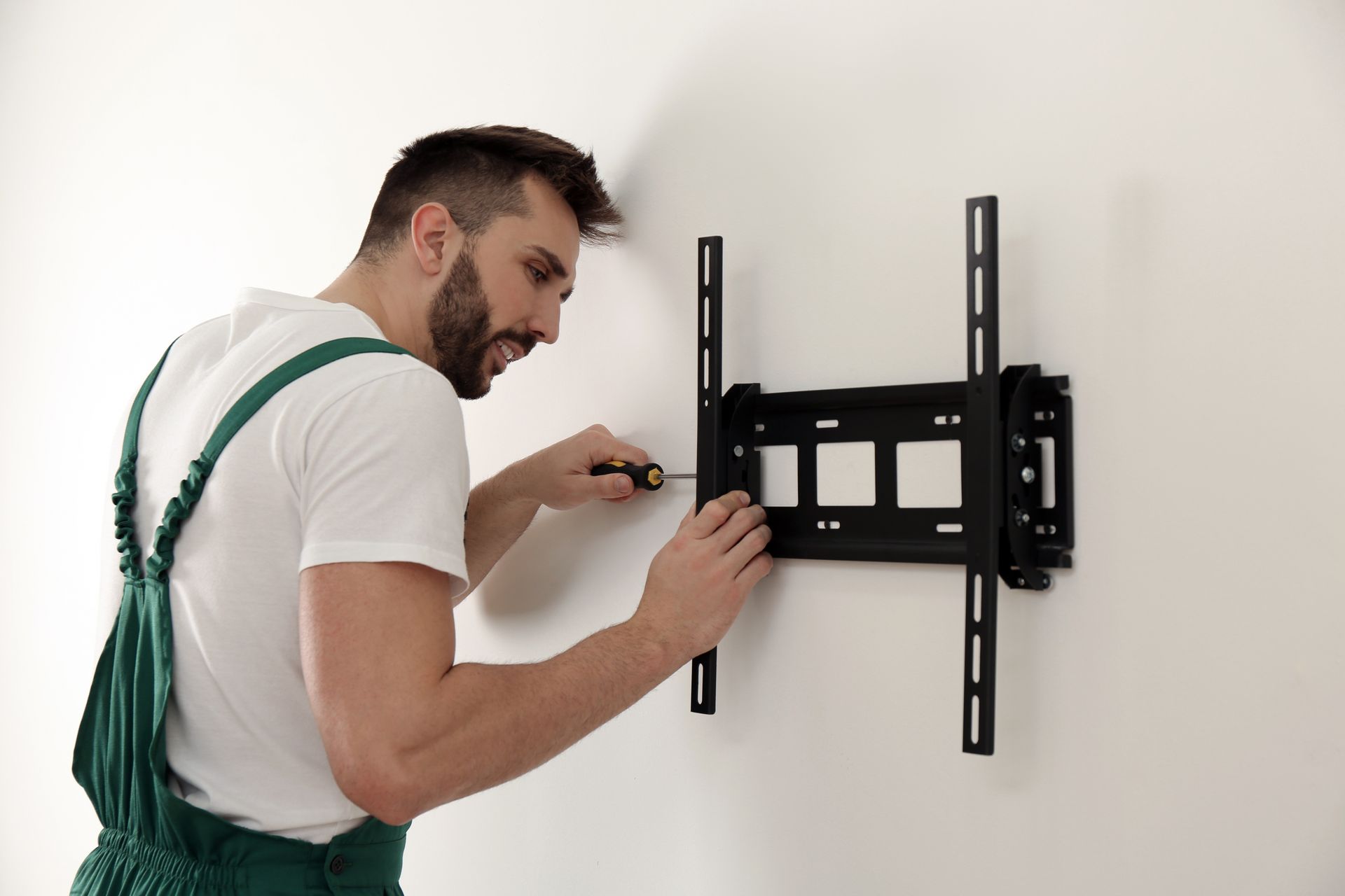 Man installing a black TV wall mount with a drill on a white wall