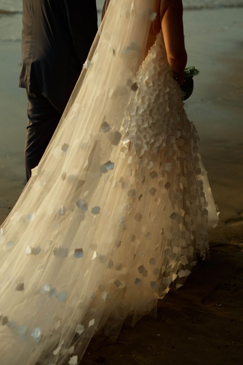 A cauda de um vestido creme com lantejoulas se arrastava pelo chão ao lado das pernas de uma pessoa.
