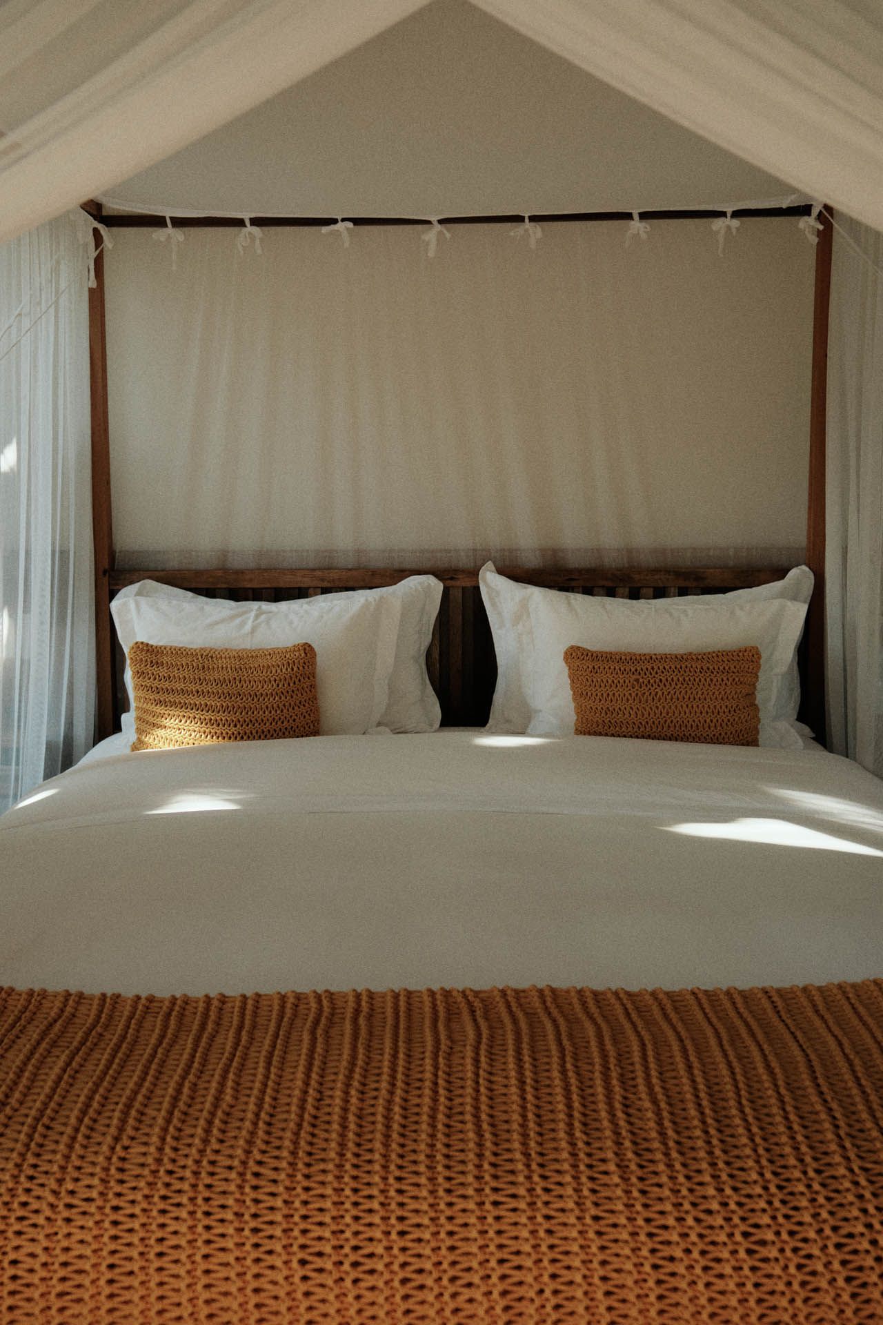 Cama aconchegante em um quarto com cobertura branca, com travesseiros e manta de tecido.