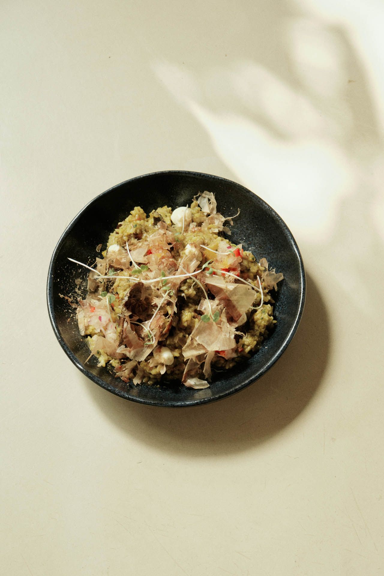 Uma tigela preta com comida variada sobre uma mesa clara, com sombras suaves ao redor.