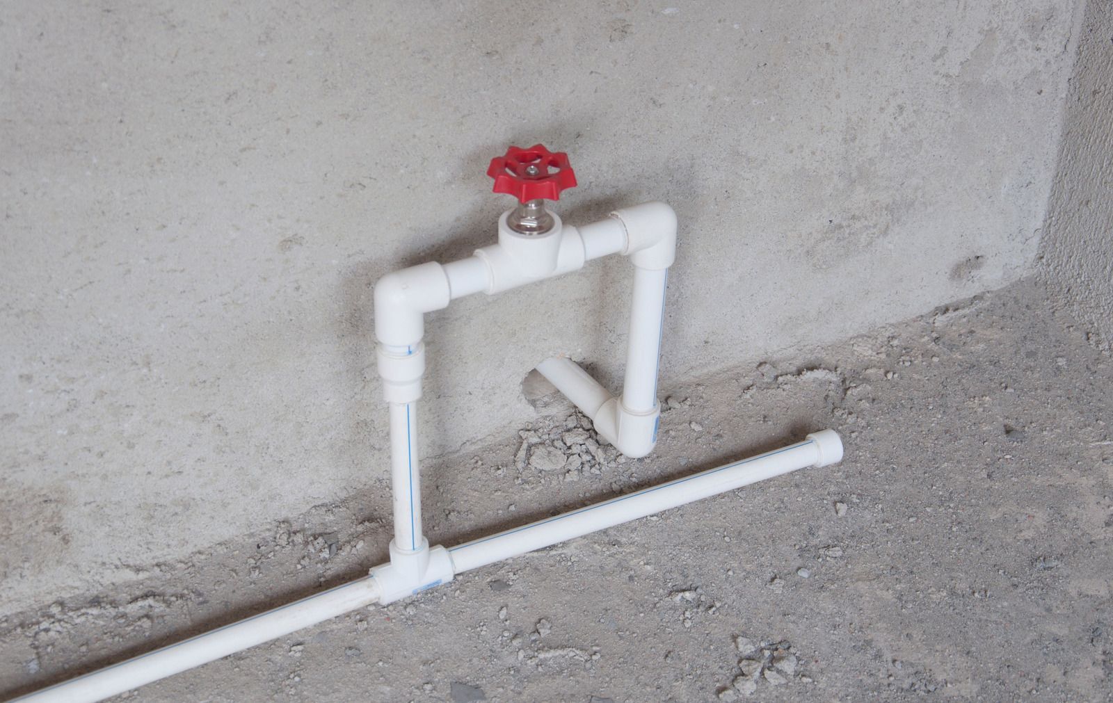 White PVC pipes with a red valve mounted against a concrete wall