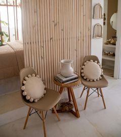 Two beige chairs face a wooden slat wall; a small table holds a white vase.
