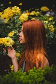 Woman with auburn hair smelling yellow flowers in a lush garden.