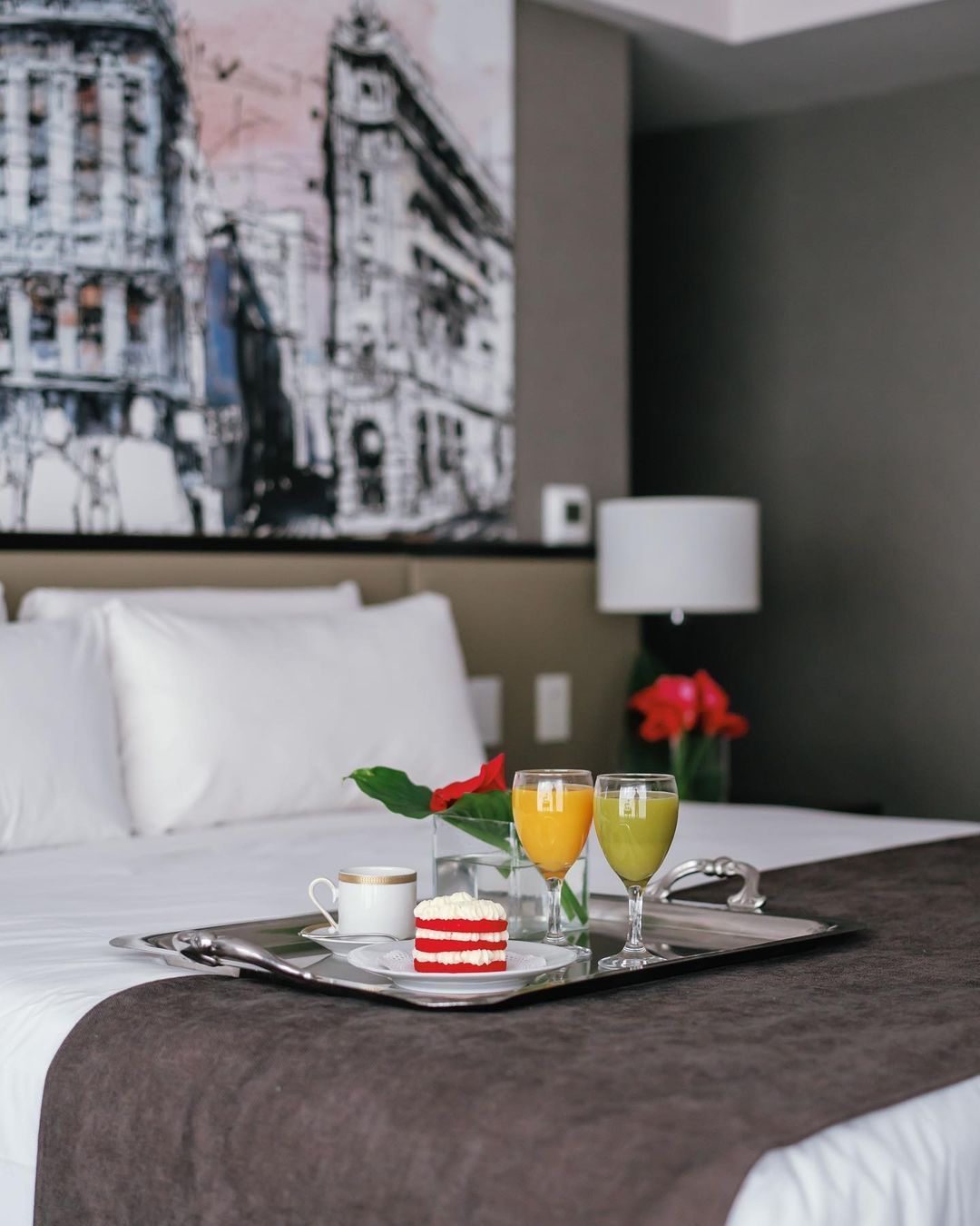 Una habitación de hotel con una bandeja de comida y bebidas en la cama.