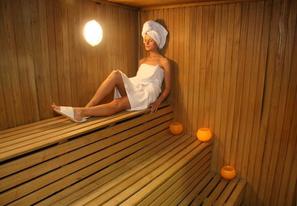 Una mujer envuelta en una toalla está sentada en una sauna de madera.