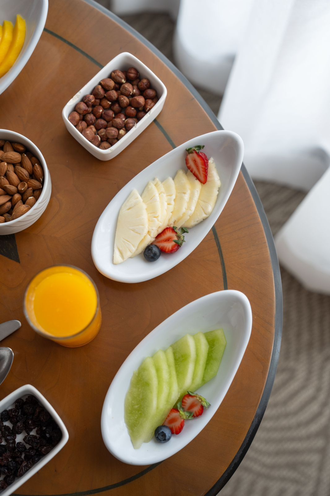 Una mesa cubierta con platos de fruta, nueces y un vaso de jugo de naranja.