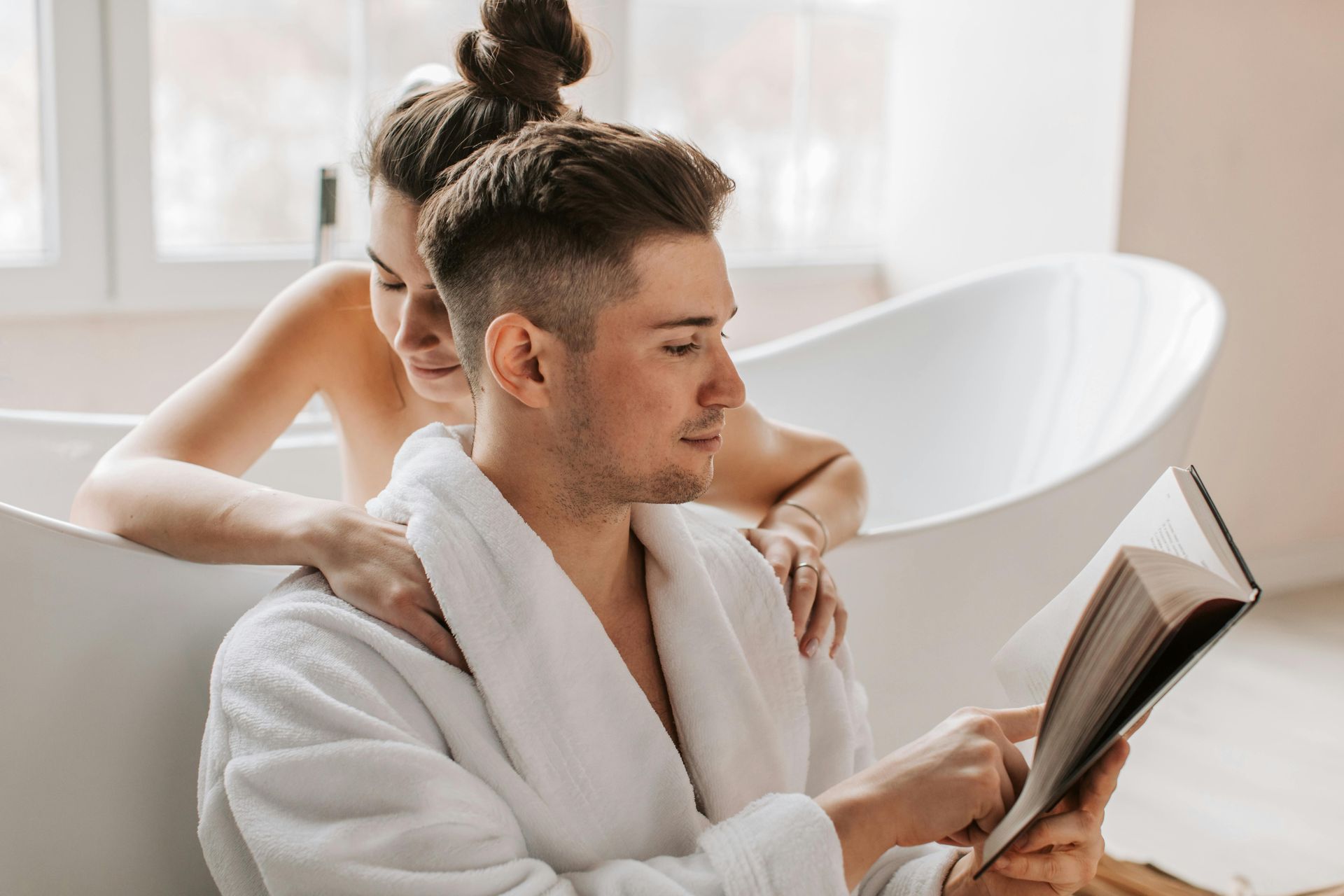 Un hombre está leyendo un libro mientras una mujer se está bañando.