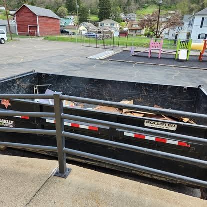 A dumpster is sitting in a parking lot next to a fence.