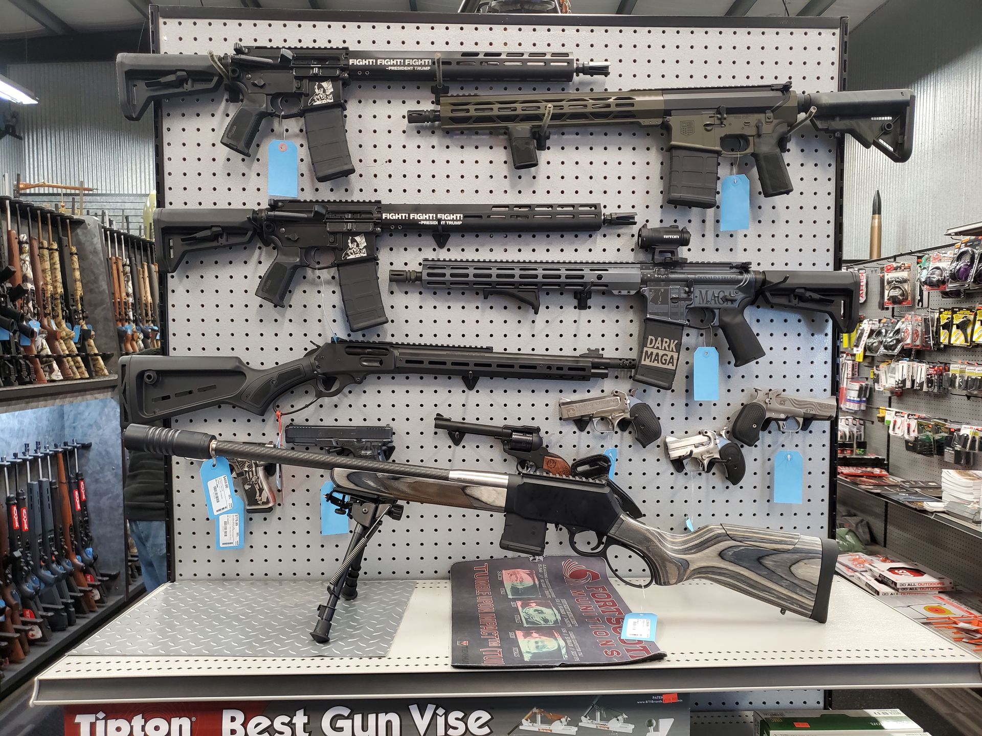 Firearms displayed on a wall. Multiple rifles with scopes and magazines are visible.